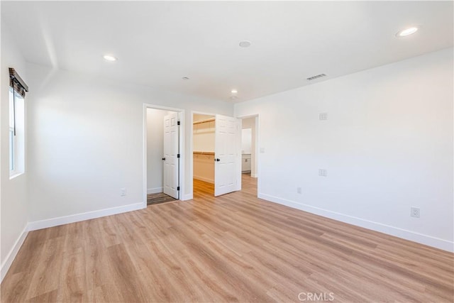 unfurnished bedroom featuring light wood-type flooring, a spacious closet, and a closet