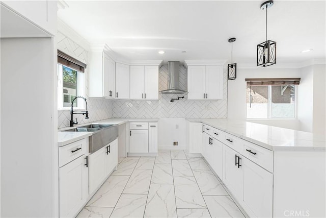 kitchen with white cabinetry, sink, wall chimney exhaust hood, light stone countertops, and decorative light fixtures