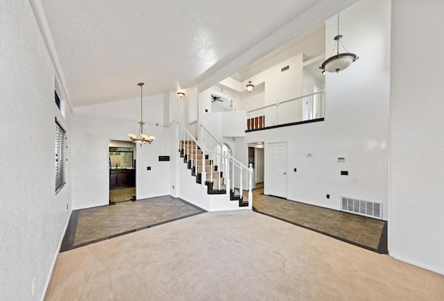 unfurnished living room featuring a chandelier, a textured ceiling, carpet floors, and high vaulted ceiling