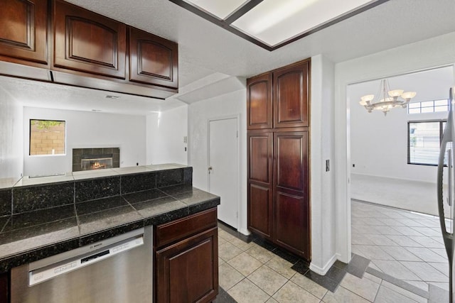 kitchen featuring a tile fireplace, dishwasher, light tile patterned flooring, and an inviting chandelier