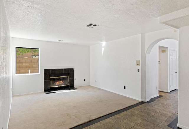 unfurnished living room featuring a tiled fireplace, carpet floors, and a textured ceiling