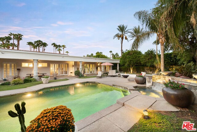 pool at dusk with a patio and a hot tub