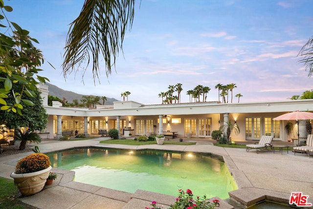 pool at dusk featuring ceiling fan, a mountain view, a patio, and french doors