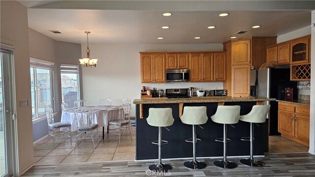 kitchen featuring hanging light fixtures, a kitchen island with sink, stainless steel appliances, a notable chandelier, and a kitchen bar