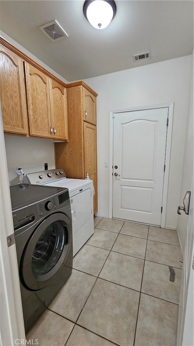 laundry room featuring light tile patterned floors, cabinets, washer and dryer, and a textured ceiling