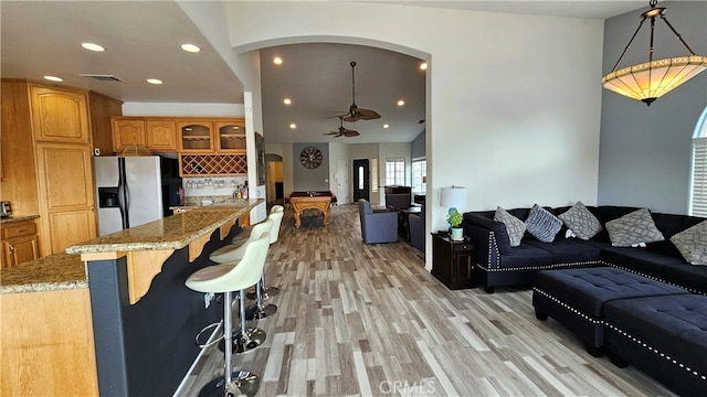 kitchen featuring light stone countertops, ceiling fan, a breakfast bar, stainless steel fridge, and light hardwood / wood-style floors