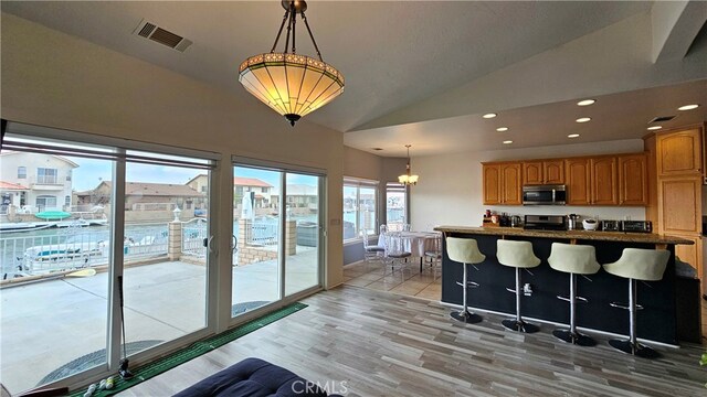 kitchen featuring lofted ceiling, light wood-type flooring, a breakfast bar area, hanging light fixtures, and appliances with stainless steel finishes