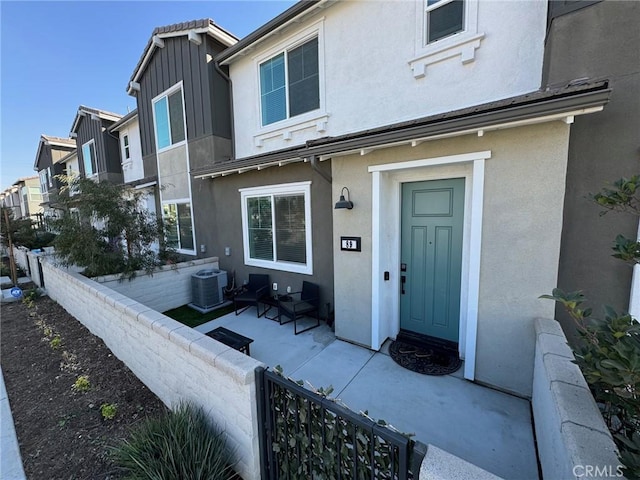 entrance to property with stucco siding, fence, cooling unit, and a patio