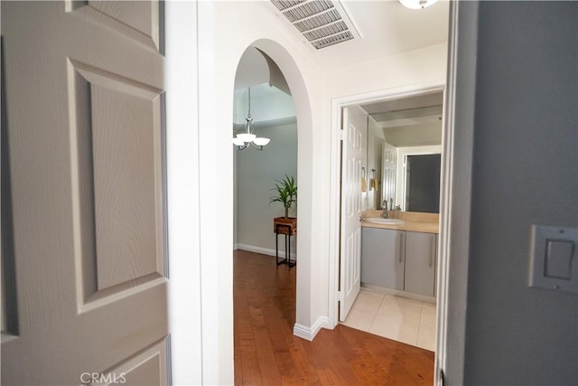 hallway with wood-type flooring, an inviting chandelier, and sink