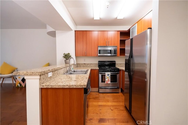 kitchen with sink, a kitchen breakfast bar, kitchen peninsula, light hardwood / wood-style floors, and appliances with stainless steel finishes