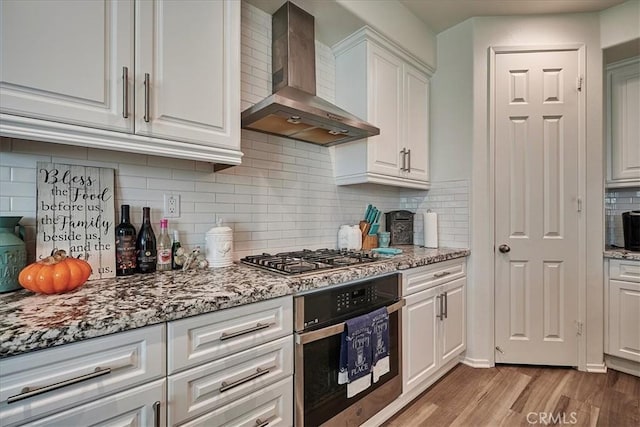 kitchen featuring light stone countertops, wall chimney exhaust hood, stainless steel appliances, light hardwood / wood-style flooring, and white cabinets