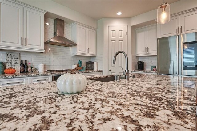 kitchen with white cabinets, wall chimney range hood, sink, and stainless steel refrigerator