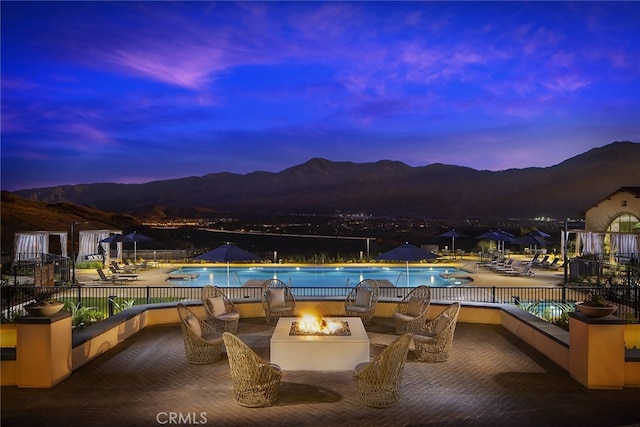 pool at dusk featuring a mountain view, a patio, and an outdoor fire pit