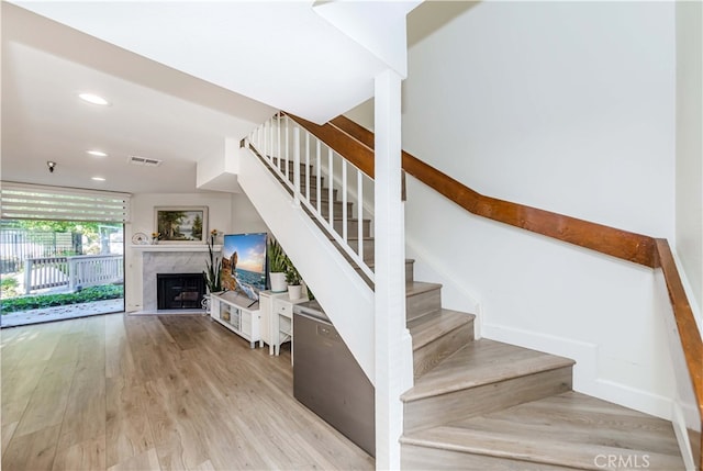 staircase featuring a high end fireplace and wood-type flooring