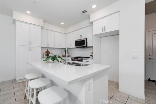 kitchen featuring stainless steel appliances, tasteful backsplash, a breakfast bar area, a kitchen island with sink, and white cabinets