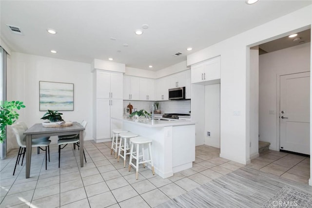 kitchen featuring sink, a kitchen breakfast bar, backsplash, an island with sink, and white cabinets