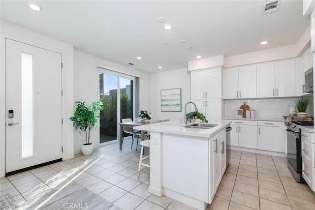 kitchen featuring decorative backsplash, stainless steel appliances, a kitchen island with sink, sink, and white cabinetry