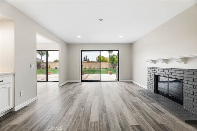 unfurnished living room featuring light hardwood / wood-style floors, a brick fireplace, and plenty of natural light