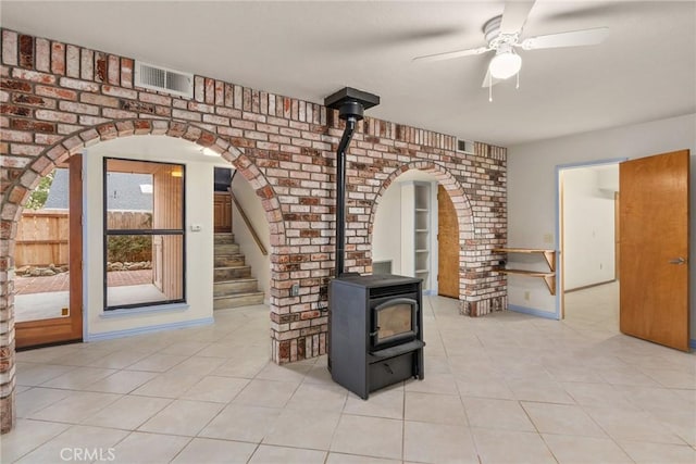 tiled living room with a wood stove, ceiling fan, and brick wall