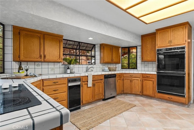 kitchen featuring decorative backsplash, black double oven, light tile patterned floors, tile countertops, and dishwasher