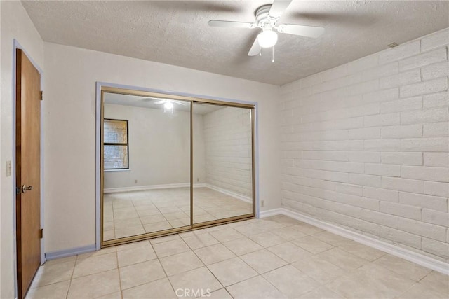 unfurnished bedroom with a textured ceiling, a closet, ceiling fan, and brick wall