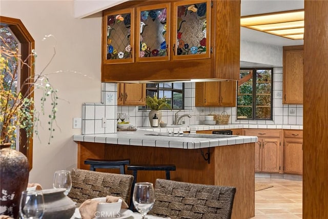 kitchen with backsplash, tile countertops, kitchen peninsula, and a breakfast bar