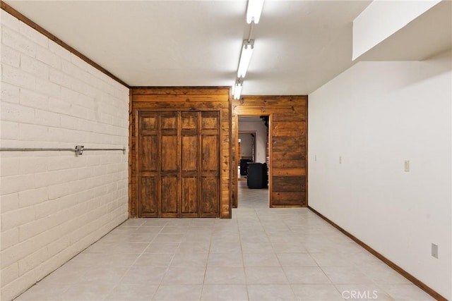 hall with wood walls, light tile patterned floors, and brick wall