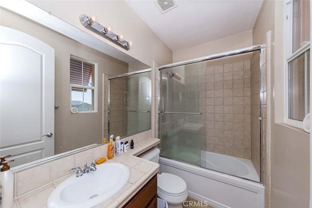 full bathroom with combined bath / shower with glass door, vanity, and toilet