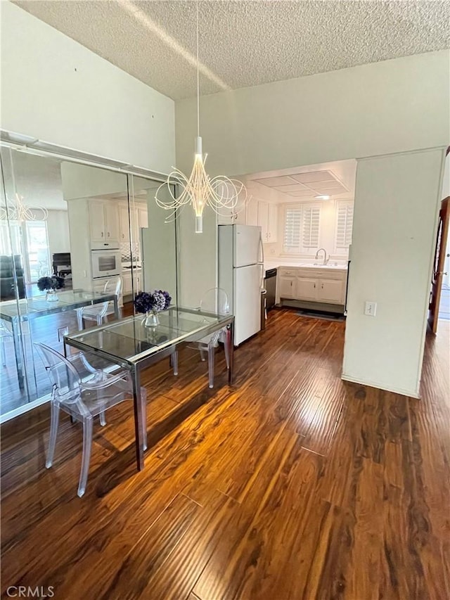 unfurnished dining area with a textured ceiling, a notable chandelier, sink, and dark wood-type flooring