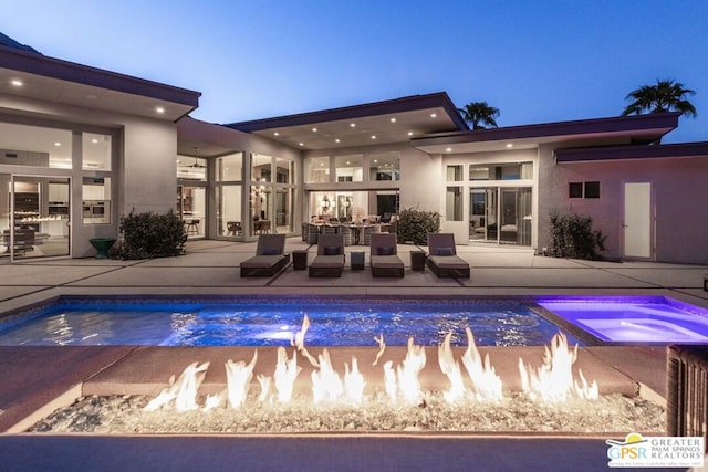 pool at dusk with an in ground hot tub and a patio area