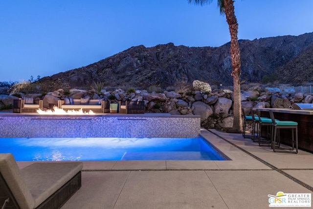 pool at dusk featuring a mountain view, a patio, and a bar