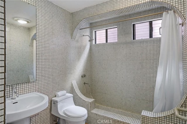 full bathroom with tiled shower, a sink, tile walls, and toilet