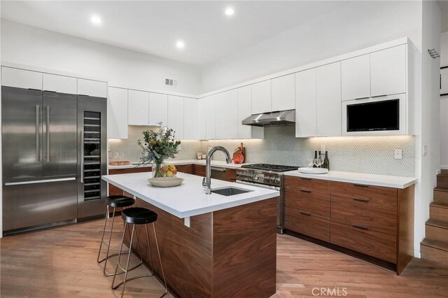 kitchen featuring sink, light hardwood / wood-style flooring, extractor fan, a center island with sink, and high end appliances