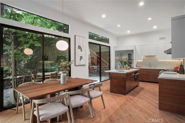 kitchen featuring white cabinetry, an island with sink, a healthy amount of sunlight, and decorative light fixtures