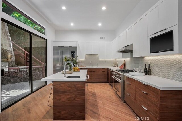 kitchen with high quality appliances, a kitchen island with sink, sink, light hardwood / wood-style floors, and a kitchen bar