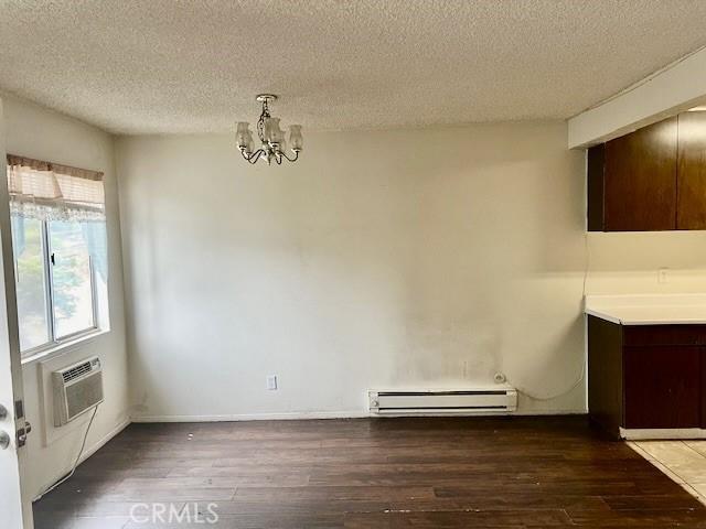 unfurnished dining area featuring an inviting chandelier, a baseboard radiator, dark hardwood / wood-style floors, and a textured ceiling