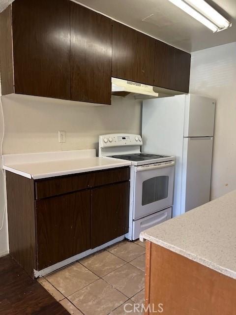 kitchen with dark brown cabinets, light tile patterned floors, and white appliances