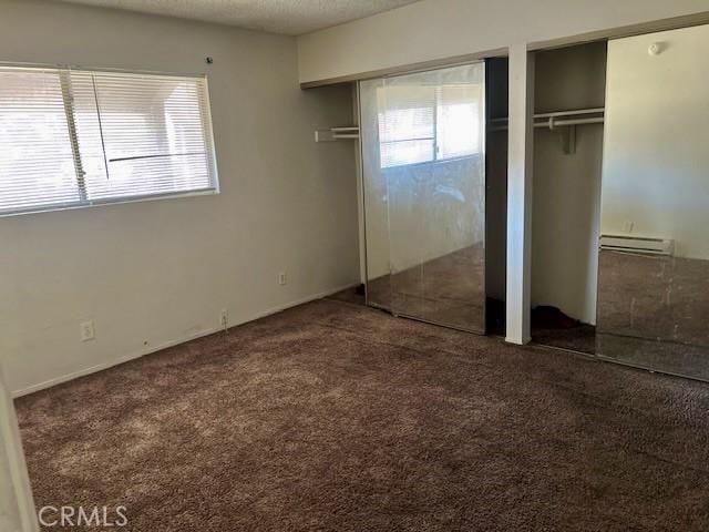 unfurnished bedroom with multiple windows, dark carpet, two closets, and a baseboard radiator