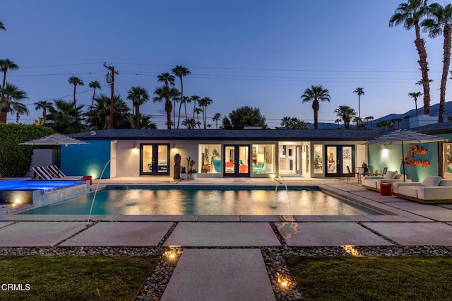 pool at dusk with a patio area, an in ground hot tub, french doors, and pool water feature