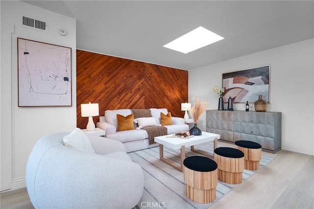 living room with light hardwood / wood-style floors, a skylight, and wood walls