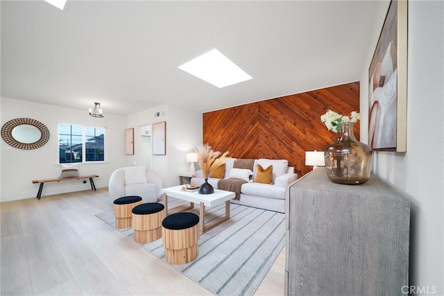 living room featuring light wood-type flooring, a skylight, and wooden walls