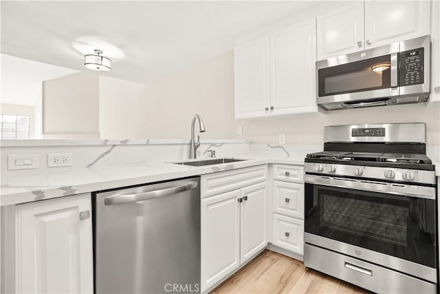 kitchen featuring white cabinets, appliances with stainless steel finishes, light hardwood / wood-style flooring, sink, and light stone counters