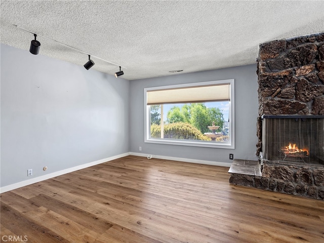 unfurnished living room with rail lighting, a stone fireplace, wood-type flooring, and a textured ceiling