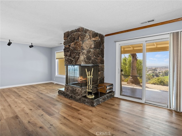 unfurnished living room featuring a multi sided fireplace, a textured ceiling, a healthy amount of sunlight, and wood-type flooring