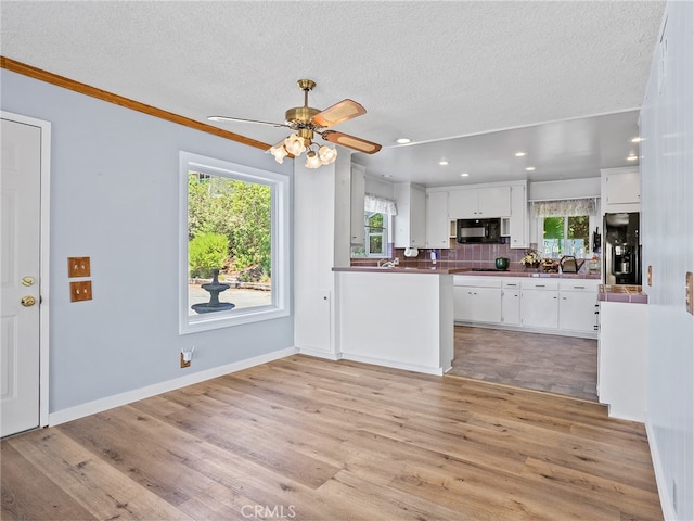 kitchen featuring black appliances, white cabinets, light hardwood / wood-style flooring, and a textured ceiling