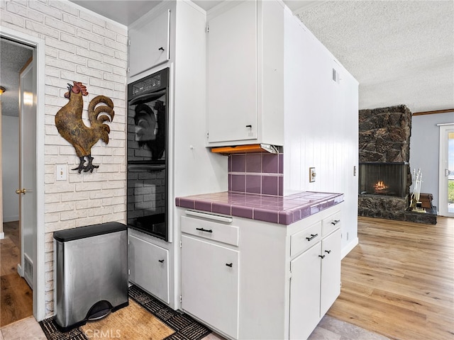 kitchen featuring tile countertops, a stone fireplace, light hardwood / wood-style flooring, and white cabinets