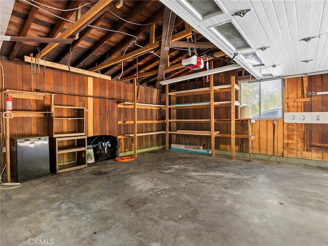 garage with a garage door opener, wooden walls, and stainless steel refrigerator