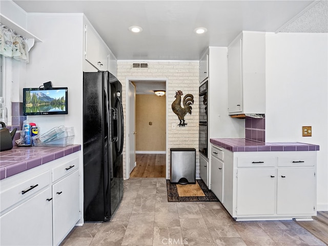 kitchen featuring black refrigerator with ice dispenser, tile counters, white cabinets, and light hardwood / wood-style floors