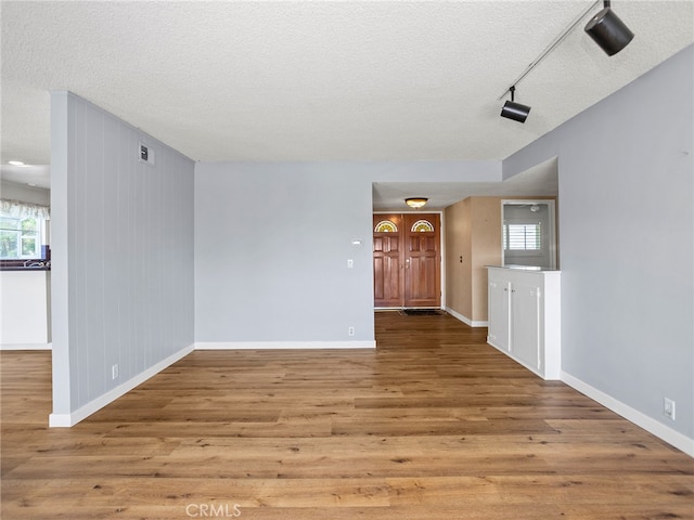 empty room featuring wood walls, a textured ceiling, and light wood-type flooring