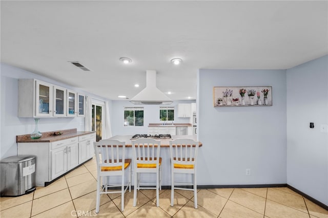 kitchen featuring white cabinets, light tile patterned floors, a kitchen bar, and ventilation hood